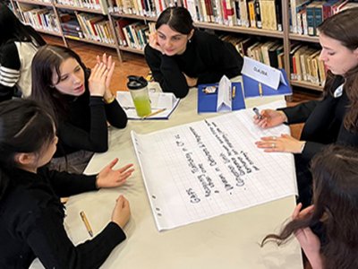 Students sit at a table in a library in Italy as one takes notes